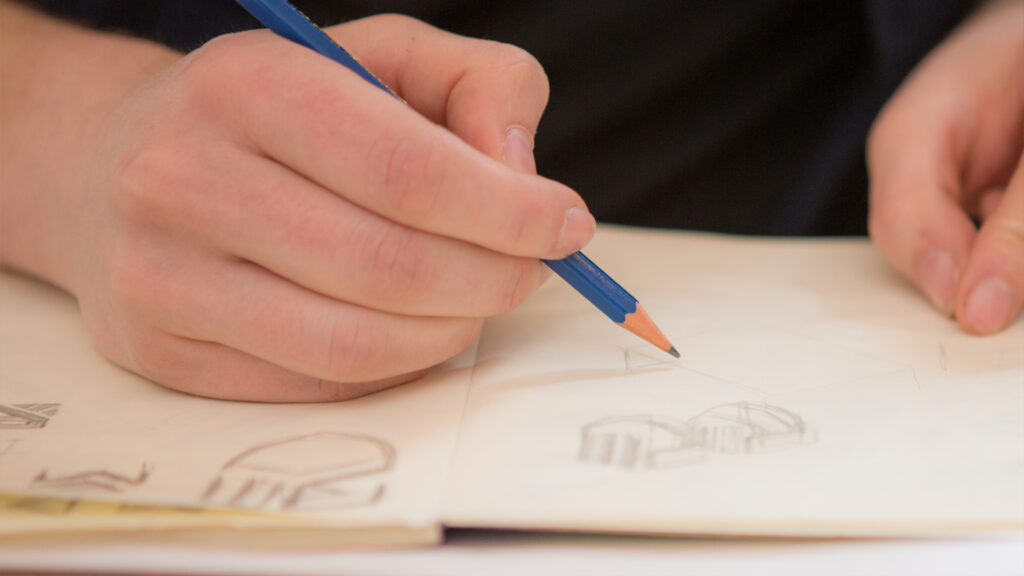Nahaufnahme von Händen, die mit einem blauen Stift Skizzen ins Notizbuch zeichnen.